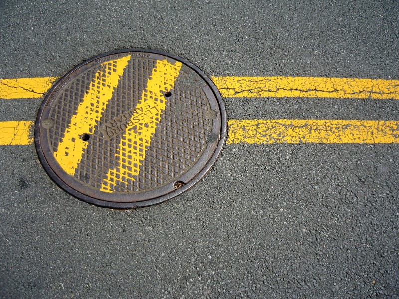 Line in the middle of a road, painted over a manhole cover that was reinstalled at a 45 degree angle instead of lined up.