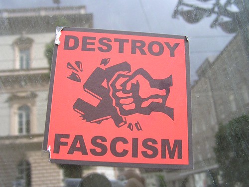 Orange sign with fist punching a swastika. “Destroy Fascism”